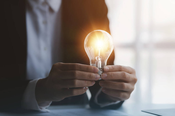 Person holding glowing lamp, Creative new idea. Innovation, brainstorming, strategizing to make the business grow and be profitable. Concept execution, strategy planning and profit management. - Photo, image