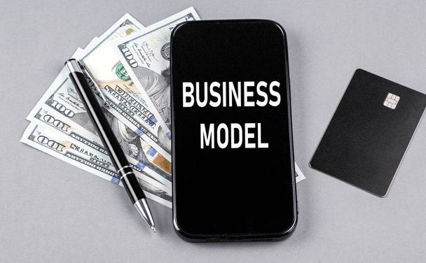 Credit card and text BUSINESS MODEL on smartphone with dollars and pen. Business - Zdjęcie, obraz