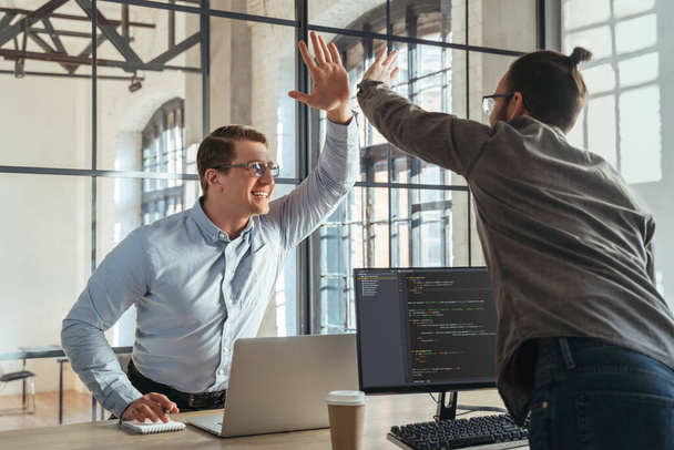 Colleagues coders giving high five to each other celebrating successful start-up launch. Programmers rejoice at the successful launch of their product. - Foto, Bild
