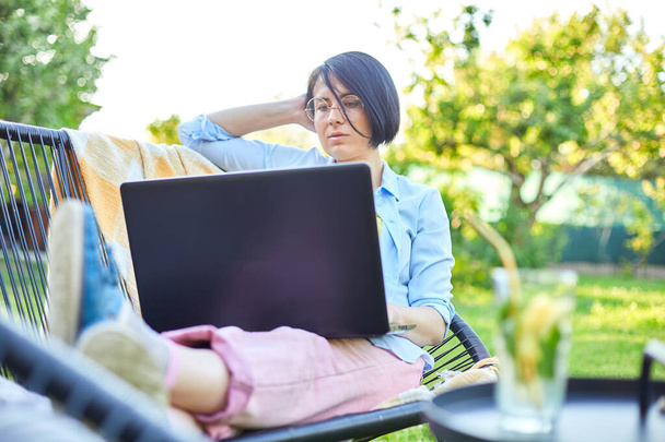 Freelance nainen työskentelee kannettavan tietokoneen kotona takapihalla, käsite etätyön mukava ulkona työtila, tarkistaa sosiaalisen median, ostoksia verkossa, tilaaminen toimitus puutarhassa. - Valokuva, kuva