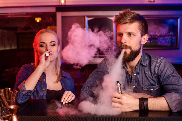 Um homem e uma mulher a fumar cigarros electrónicos num bar. Vape shop - Foto, Imagem