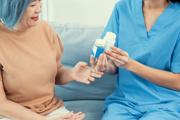 Caregiver advising contented senior woman on medication in the living room. Medication for seniors, nursing house, healthcare at home. - Foto, imagen