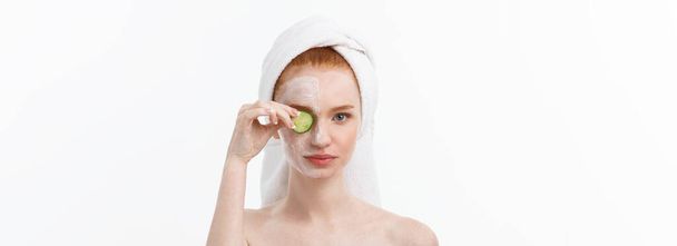 Aantrekkelijke jonge vrouw met mooie, schone huid. Wit masker en komkommers. Schoonheidsbehandelingen en cosmetologie spa therapie. Witte achtergrond. - Foto, afbeelding