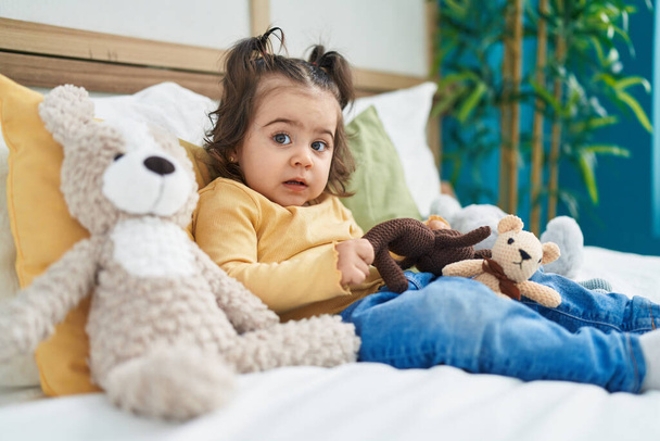 Adorável menina hispânica brincando com boneca sentada na cama no quarto - Foto, Imagem