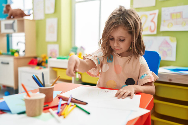 Entzückende hispanische Studentin zeichnet auf Papier, die im Kindergarten auf dem Tisch sitzt - Foto, Bild
