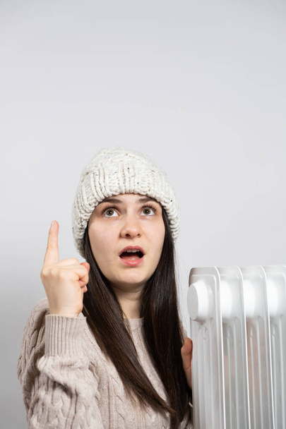 Een vrouw met een hoed warm worden in de buurt van de oliekachel en kijkt en wijst omhoog met haar vinger - Foto, afbeelding