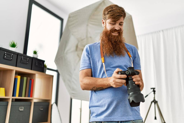 写真スタジオでプロのカメラを使用して若い赤毛の男の写真家 - 写真・画像