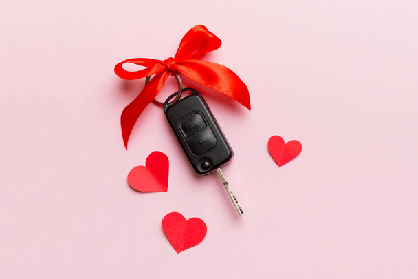 Autosleutel met een rode strik en een hartje op de gekleurde tafel. Cadeau of cadeau geven voor Valentijnsdag of kerst, Bovenaanzicht met kopieerruimte. - Foto, afbeelding