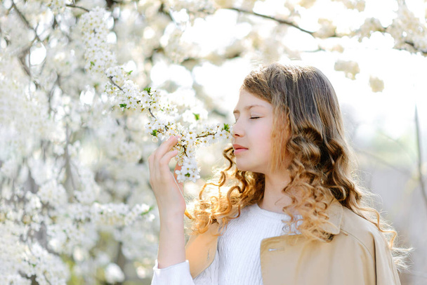 Όμορφη έφηβη κοπέλα μυρίζοντας λουλούδια και απολαμβάνοντας ζεστό ηλιόλουστο καιρό άνοιξη στην ύπαιθρο - Φωτογραφία, εικόνα