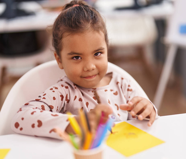 Adorable hispanic girl student sitting on table drawing on paper at kindergarten - Valokuva, kuva