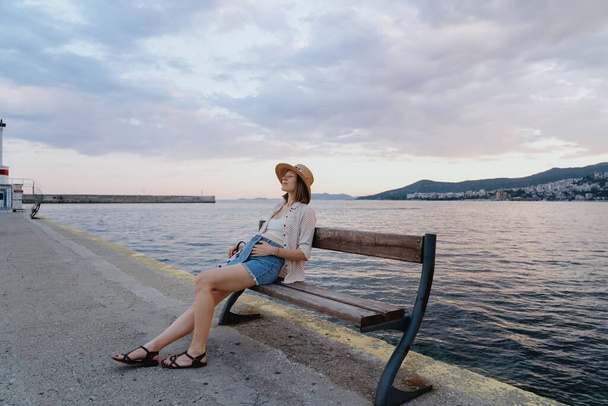 Femme enceinte à un stade précoce reposant sur un banc près de la mer le matin. Mode de vie sain, voyage et détente - Photo, image