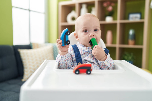 Suloinen valkoihoinen vauva imee auton lelu istuu syöttötuolilla kotona - Valokuva, kuva
