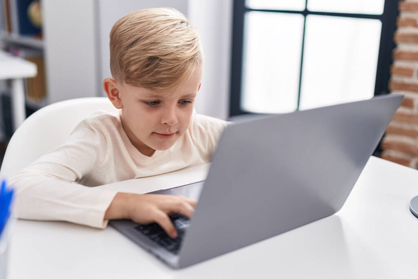 Suloinen lapsi opiskelija käyttää kannettavaa tietokonetta istuu pöydällä luokkahuoneessa - Valokuva, kuva