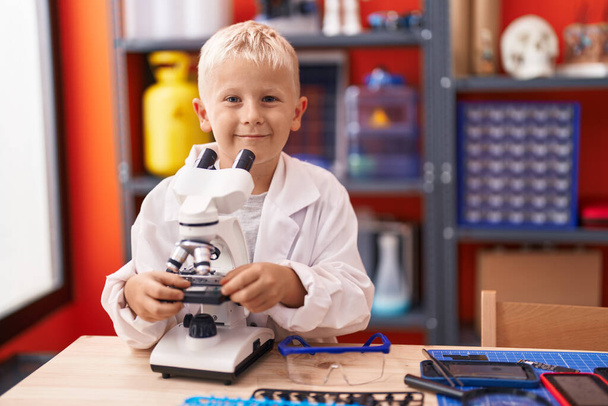 Adorable toddler student using microscope standing at classroom - Foto, immagini