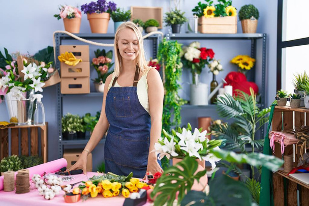 Young blonde woman florist make bouquet of flowers at florist store - Foto, afbeelding