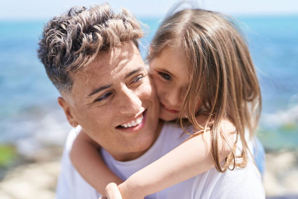 Padre e hija sonriendo confiados abrazándose unos a otros sosteniéndose en la orilla del mar - Foto, Imagen