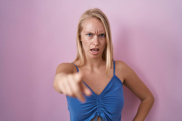 Nuori valkoihoinen nainen seisoo vaaleanpunainen tausta osoittaa tyytymätön ja turhautunut kameraan, vihainen ja raivoissaan sinulle  - Valokuva, kuva