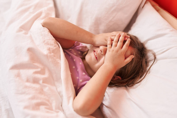 Adorável menina hispânica estressado com as mãos nos olhos deitado na cama no quarto - Foto, Imagem