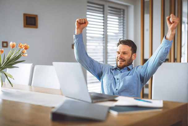 Excited caucasian man cheering for his team, watching a football game on his laptop, man celebrating a win with clenched fists.  - Photo, image
