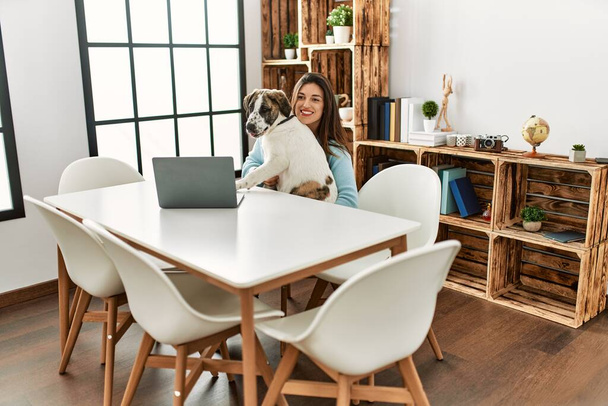 Jeune femme et chien utilisant un ordinateur portable assis sur la table à la maison - Photo, image