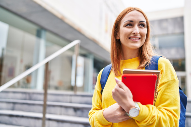 Young caucasian woman student smiling confident holding books at university - 写真・画像