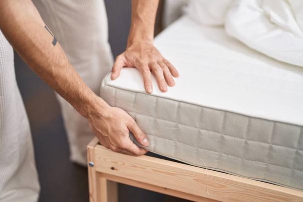 Young hispanic man holding mattress at bedroom - 写真・画像