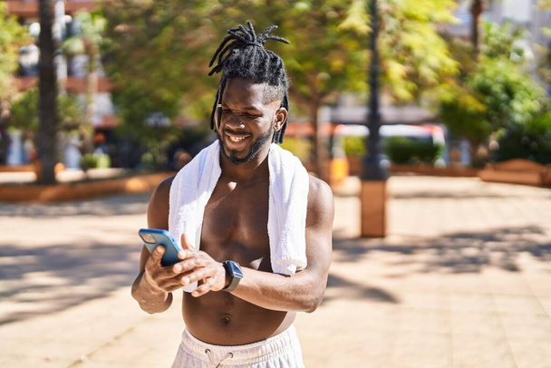 African american woman shirtless smiling confident using smartphone at park - Photo, Image
