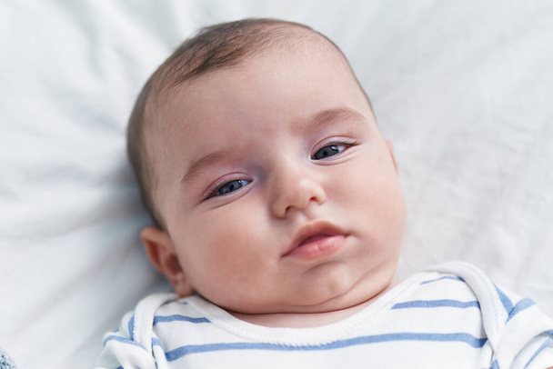 Adorable caucasian baby lying on bed with relaxed expression at bedroom - Φωτογραφία, εικόνα