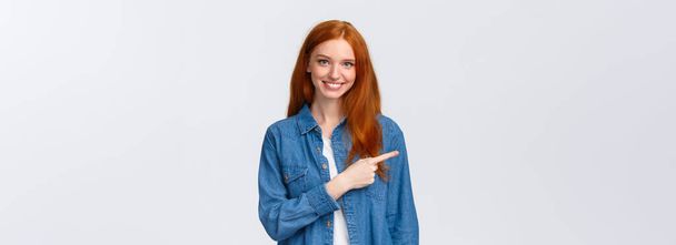 Here what need. Cheerful redhead woman in denim shirt, pointing finger left copy space, smiling recommend good product, review service, indicating website, standing white background. - Photo, Image