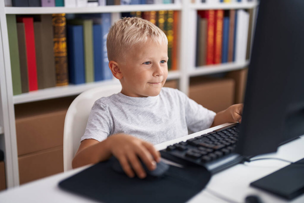 Чарівний учень малюка, використовуючи комп'ютер, що сидить на столі в класі
 - Фото, зображення