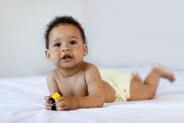Tummy Time. Cute Black Little Baby Lying On Bed At Home, Closeup Shot Of Adorable Sweet African American Infant Child In Diaper Playing With Car Toy While Relaxing In White Bedroom, Free Space - Foto, imagen
