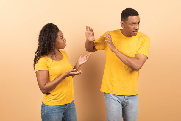 アフリカ系アメリカ人のカップルは、怒り狂った黒人女性が彼女を無視し、黄色のスタジオの背景の上に立っていらいらするボーイフレンドに叫んでいると主張した。関係問題の概念 - 写真・画像