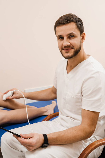 Leg ultrasound examination before surgery. Vascular surgeon examines arteries and veins of legs using portable ultrasound machine - Photo, Image
