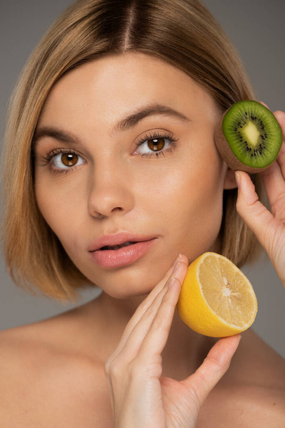портрет молодой женщины с фруктами киви и лимоном, изолированными на сером  - Фото, изображение