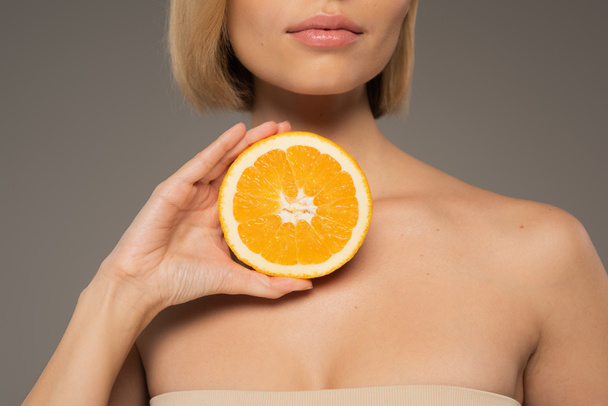 cropped view of young woman with bare shoulders holding juicy orange isolated on grey  - Foto, Imagen