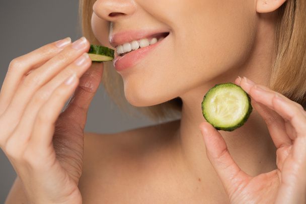 cropped view of cheerful woman holding sliced cucumbers isolated on grey  - Photo, Image