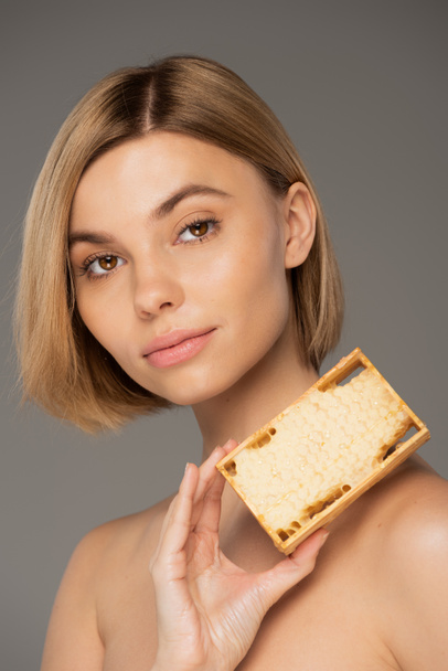 blonde young woman holding wooden frame with sweet honey isolated on grey  - Foto, afbeelding