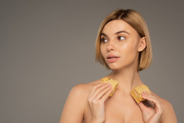 young woman with naked shoulders holding sweet honeycombs isolated on grey - Foto, Imagem