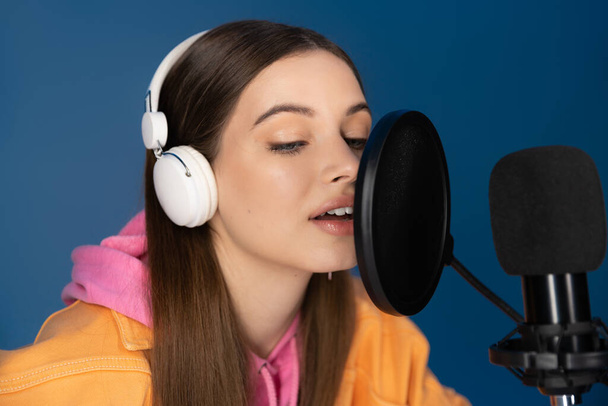 Brunette teenager in headphones talking during podcast isolated on blue  - Fotografie, Obrázek