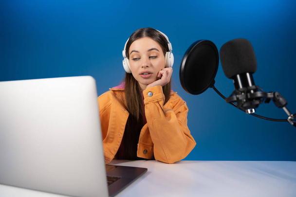Teenager in headphones looking at laptop while recording podcast isolated on blue  - Foto, imagen