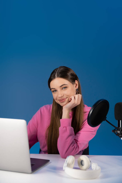 Positive teenager looking at camera near podcast microphone and laptop isolated on blue  - Foto, immagini