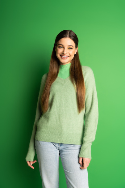 Positive teenager in jeans and jumper looking at camera on green background  - Foto, Imagem