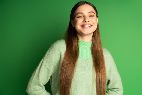 Ευτυχισμένο έφηβο κορίτσι σε jumper κοιτάζοντας κάμερα στο πράσινο φόντο  - Φωτογραφία, εικόνα