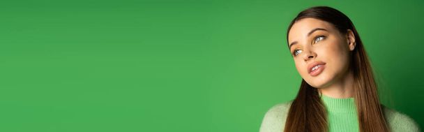 Молодая брюнетка подросток смотрит в сторону на зеленом фоне с копировальным пространством, баннер  - Фото, изображение