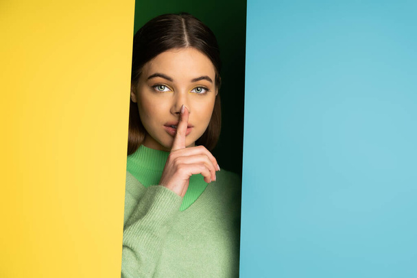 Brunette teen girl in jumper showing secret gesture on colorful background  - Foto, Imagem