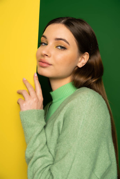 Portrait of teenager in jumper looking at camera near yellow and green background  - Fotó, kép