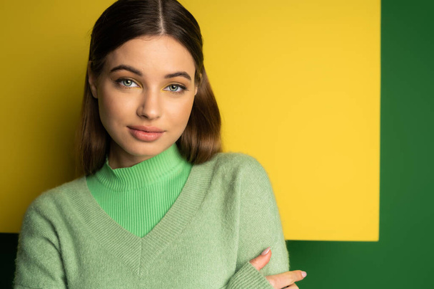 Brunette teen girl in jumper looking at camera on green and yellow background  - Foto, immagini