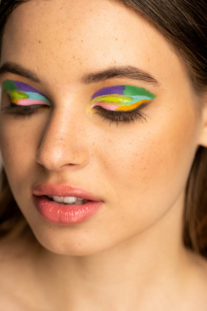 Portrait of freckled teenager with colorful eyeshadows isolated on grey  - Photo, Image