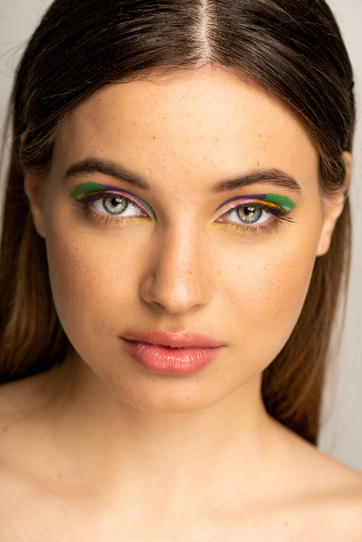 Portrait of freckled teenager with multicolored makeup standing isolated on grey  - Photo, Image