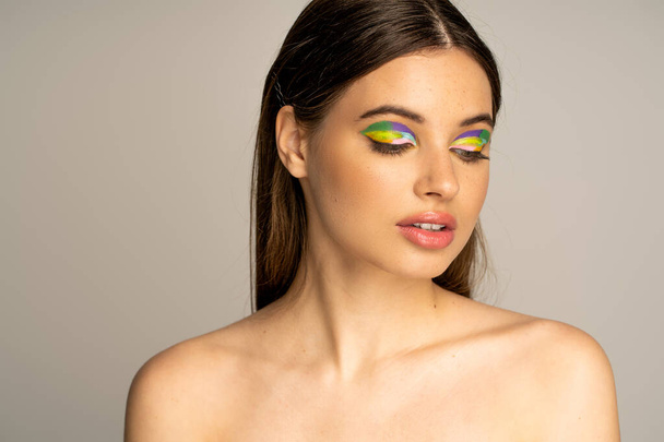 Pretty teen model with colorful visage and naked shoulders posing isolated on grey  - Photo, image